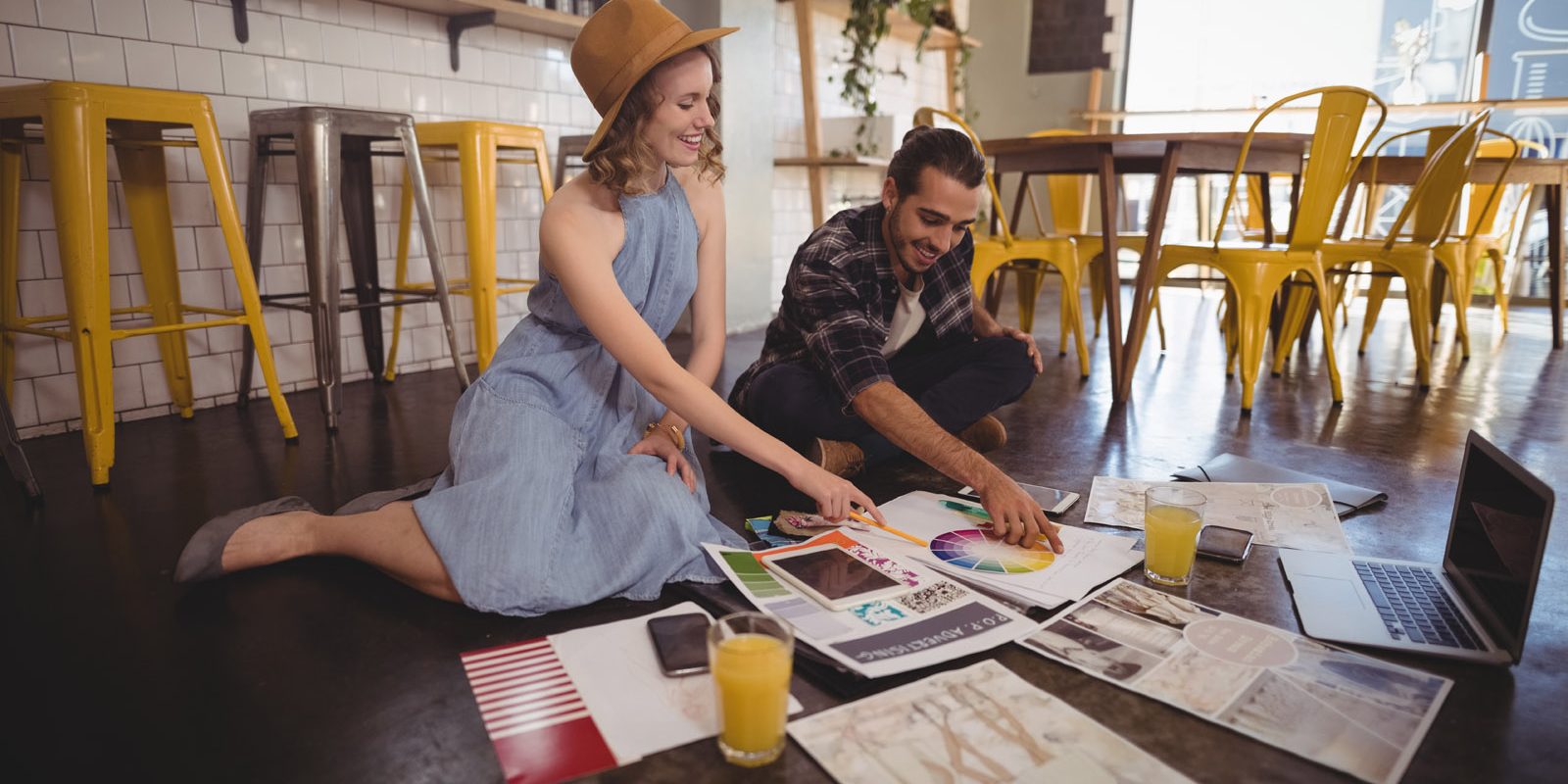 Smiling young professionals with sheets and technologies sitting on floor